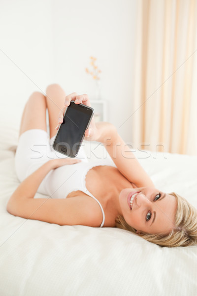Portrait of a charming woman showing her smartphone while lying on her bed Stock photo © wavebreak_media