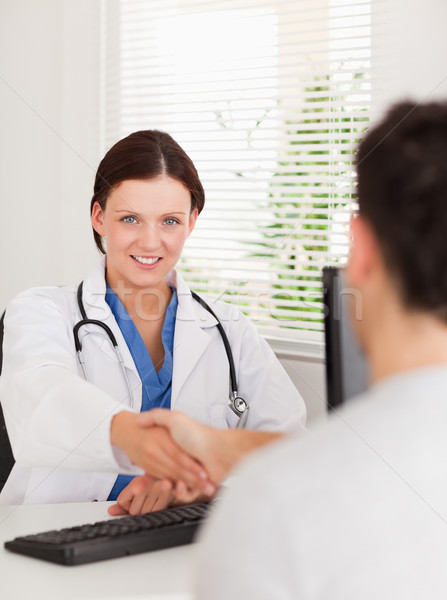 Stock photo: A female doctor is shaking hands with a patient and looking to the camera