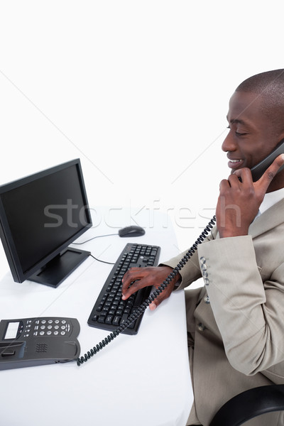 Stock photo: Side view of a male secretary answering the phone while using a computer against a white background