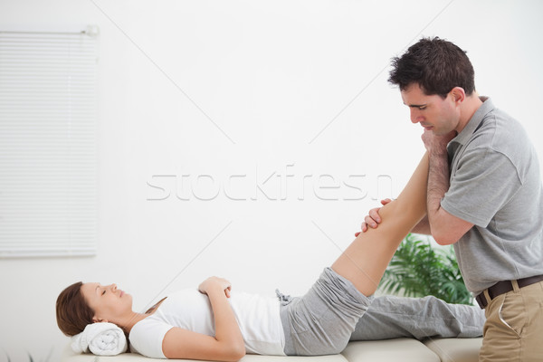 Stock photo: Chiropractor massaging a leg while placing it on his shoulder  in a room