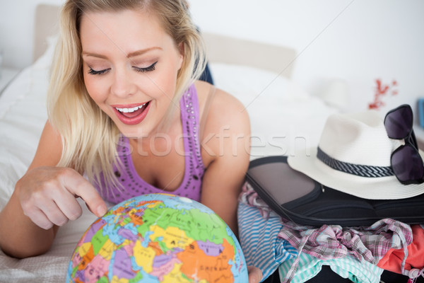 Woman with a suitcase pointing on a globe while lying on her bed Stock photo © wavebreak_media