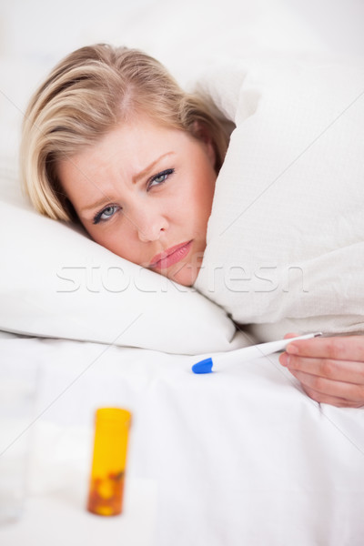 Sick young woman holding a thermometer in her bed Stock photo © wavebreak_media