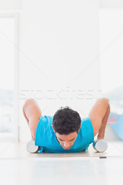 Stock photo: Man doing push ups with dumbbells in fitness studio
