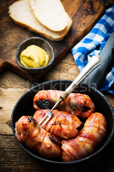 Sausages with prunes and bacon in iron pan Stock photo © zoryanchik