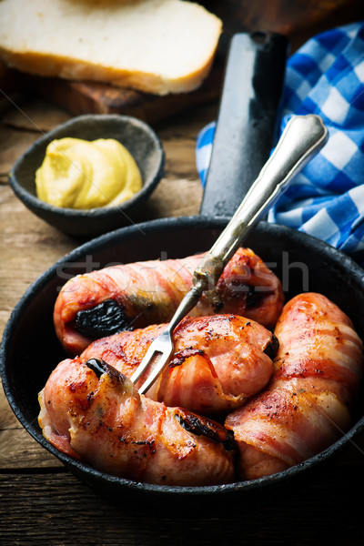 Sausages with prunes and bacon in iron pan Stock photo © zoryanchik