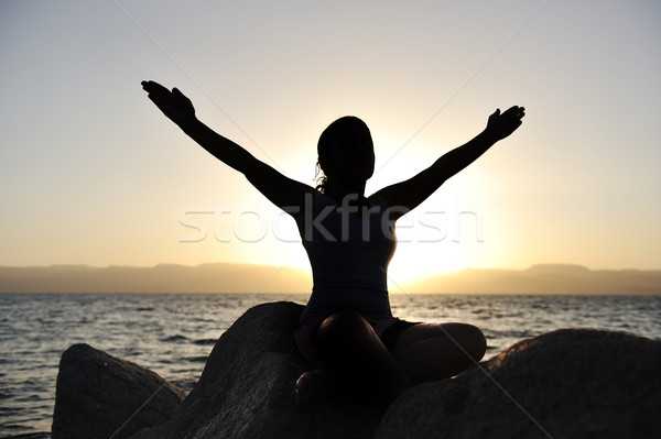 Silhouette of a beatiful female meditating on a rock by the sea Stock photo © zurijeta