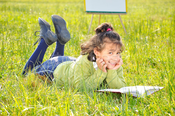 Cute girl reading on meadow with board behind Stock photo © zurijeta