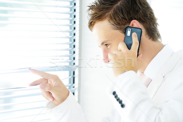 Young businessman looking through blinds whilst making call Stock photo © zurijeta