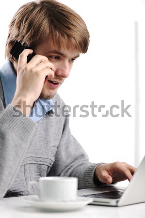 Young man speaking on cell phone and working on laptop Stock photo © zurijeta