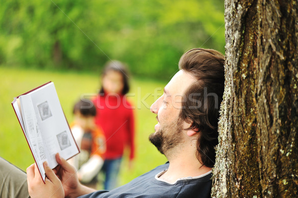 Young relaxed father reading book and children playing around Stock photo © zurijeta