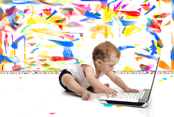 Little baby boy is sitting on floor with his laptop, isolated over white wall, in messy painted room Stock photo © zurijeta