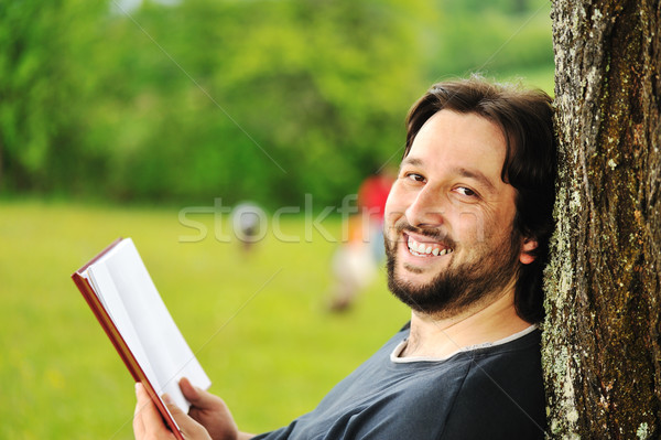 Young relaxed man reading book in nature, back on tree, meadow behind Stock photo © zurijeta