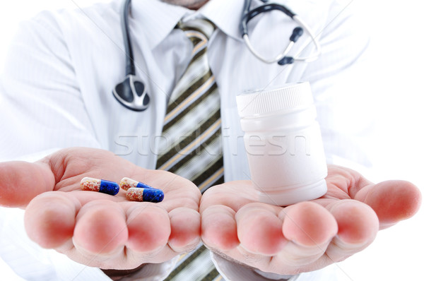 Young doctor offering pill in one and pills in bottle - in another hand. Copy space for you, for tex Stock photo © zurijeta