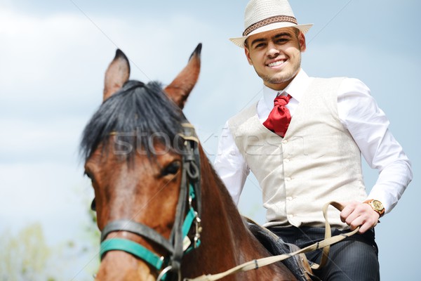 Young stylish man taking riding a horse on countryside Stock photo © zurijeta