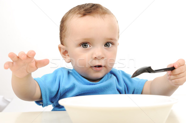 Cute adorable one year old baby with green eyes eating on table, spoon and plate Stock photo © zurijeta