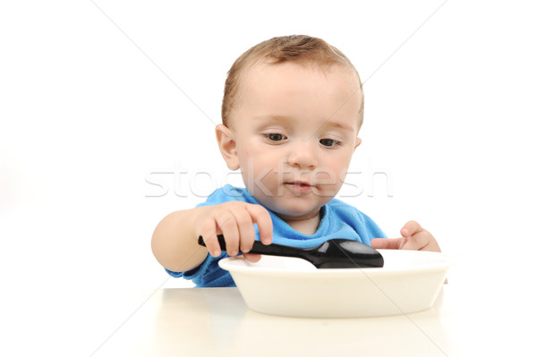 Cute adorable one year old baby with green eyes eating on table, spoon and plate Stock photo © zurijeta