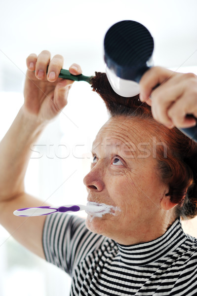 Senior woman drying hair with fan and brushing teeth Stock photo © zurijeta
